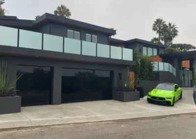 A contemporary black house with a glossy black garage door and a bright green sports car parked in the driveway.